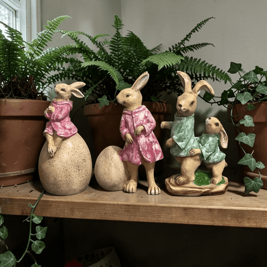 Charming bunny figurines in pink and green outfits, perfect for Easter decor or shelf styling with plants.