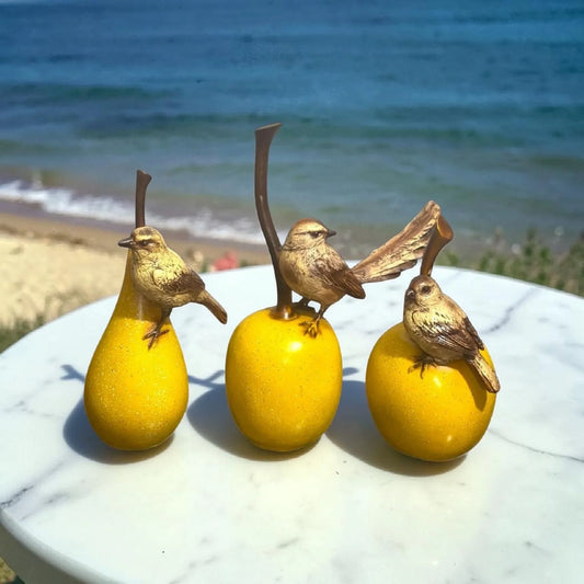 Three decorative yellow fruit figurines with small bird sculptures on a marble table by the sea