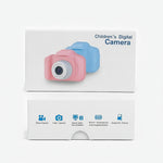 A children's digital camera shown in its retail packaging, with a pink camera and a blue camera pictured on the white box. The lower part of the box includes blue feature icons and text.